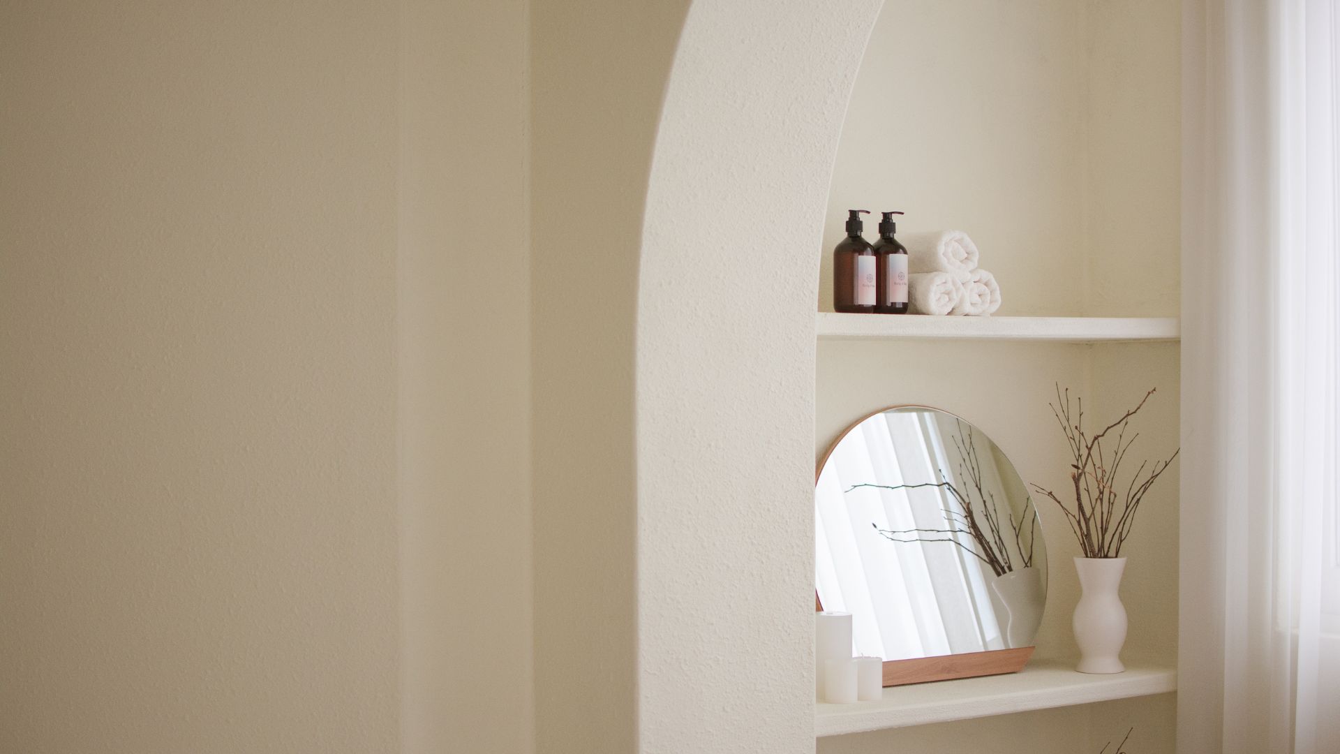 Estante blanco con un espejo y un jarrón decorativo sobre él, creando un ambiente elegante y minimalista.