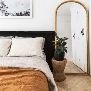 Dormitorio con cama, espejo y suelo de madera, creando un ambiente acogedor y elegante.