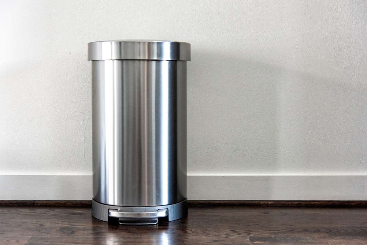 Un cubo de basura de acero inoxidable sobre un suelo de madera, destacando su diseño moderno y funcionalidad.