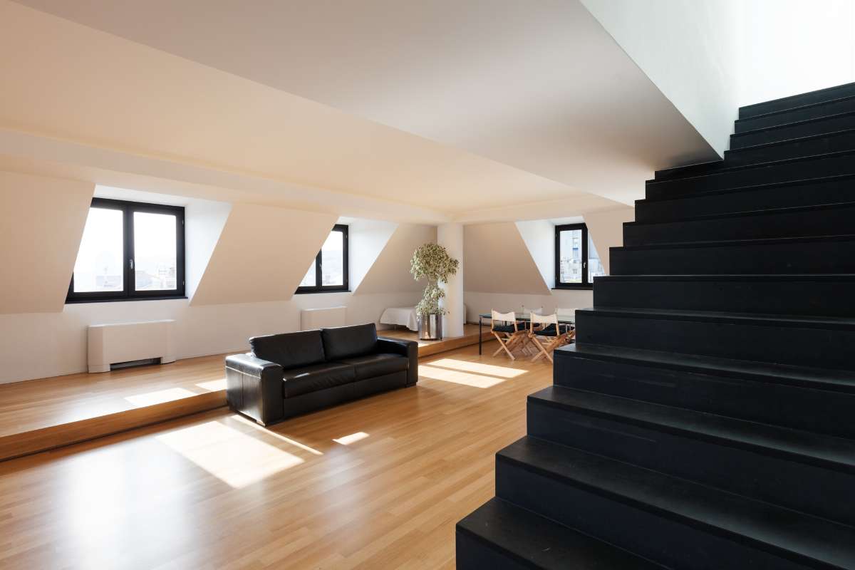 Escalera negra que conduce a un loft con paredes blancas, creando un contraste elegante y moderno en el espacio.
